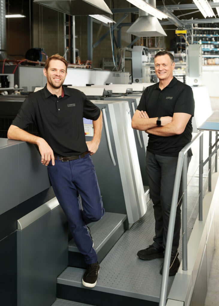 James and Glen Rowley standing in front of print machinery