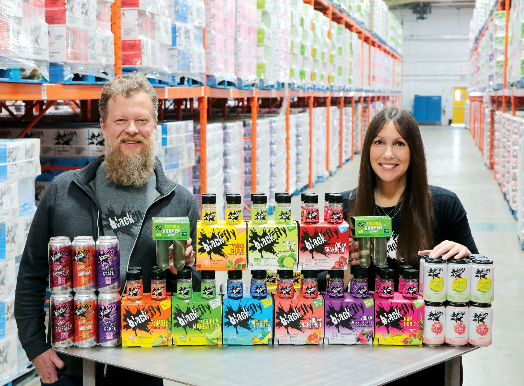 Rob Kelly and Cathy Siskind-Kelly smiling for photo with stacks of their product on a table in front of them