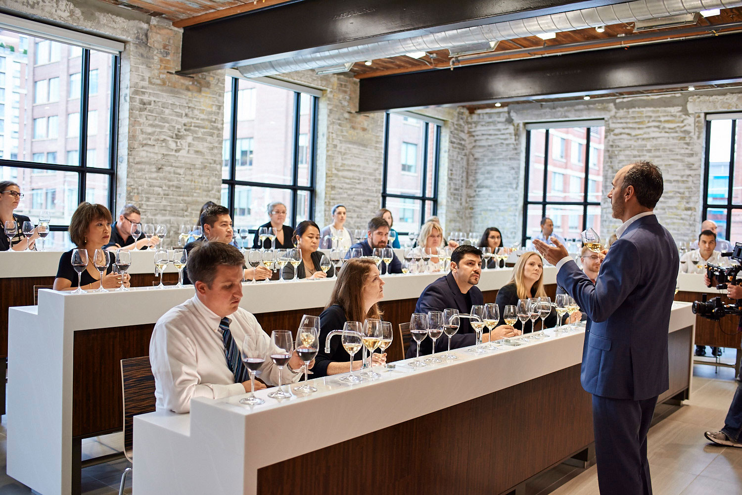 View of students with various wine samplings in front of them, listening to instructor