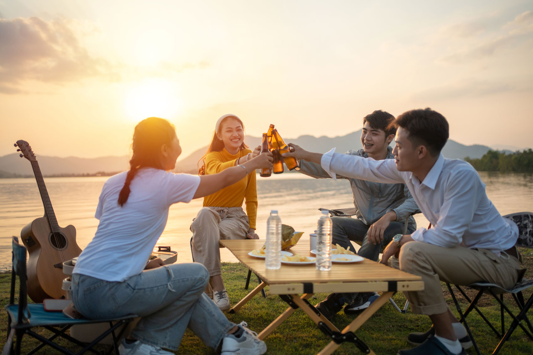Group of young adults having a beer outdoors with sun setting behind moutain landscape