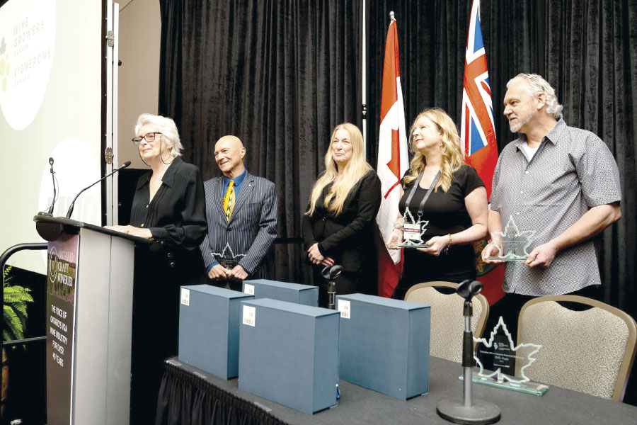 Debi Pratt standing a podium, with Donald Ziraldo, Andrea Kaiser, Magdalena Kaiser, and Gerald Klose standing in background
