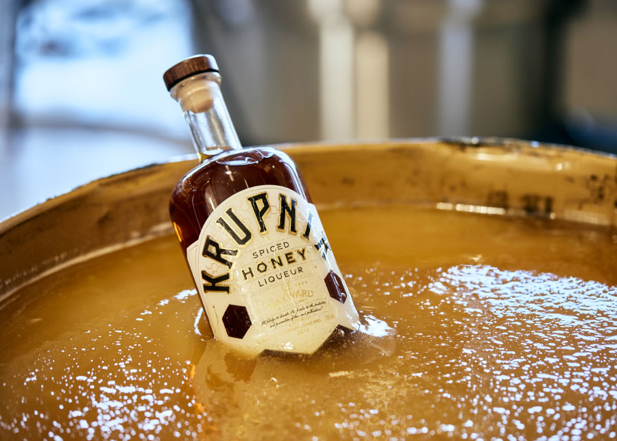 bottle of spiced honey liqueur sitting in a shallow vat of honey
