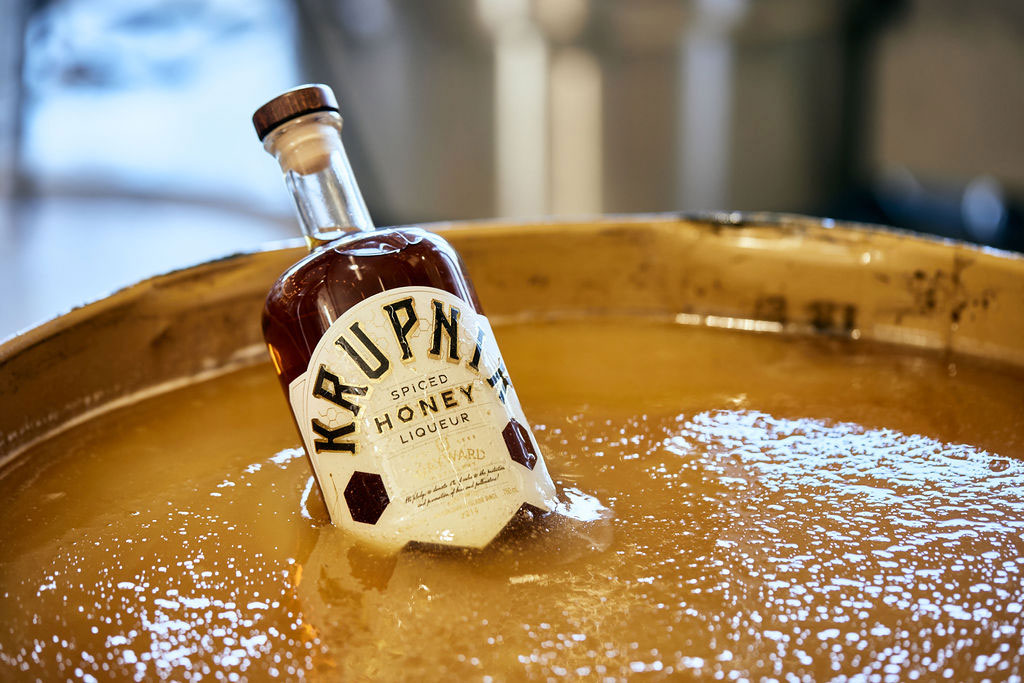 bottle of spiced honey liqueur sitting in a shallow vat of honey