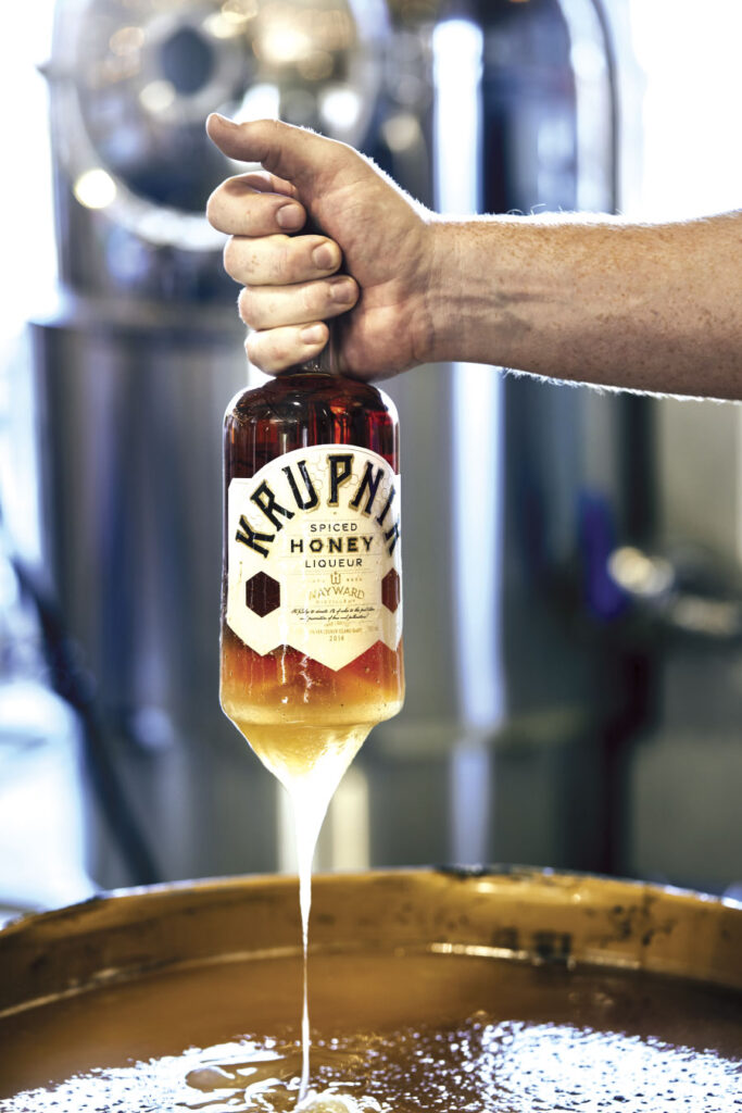 person lifting a bottle of spiced honey liqueur out of a vat filled with honey