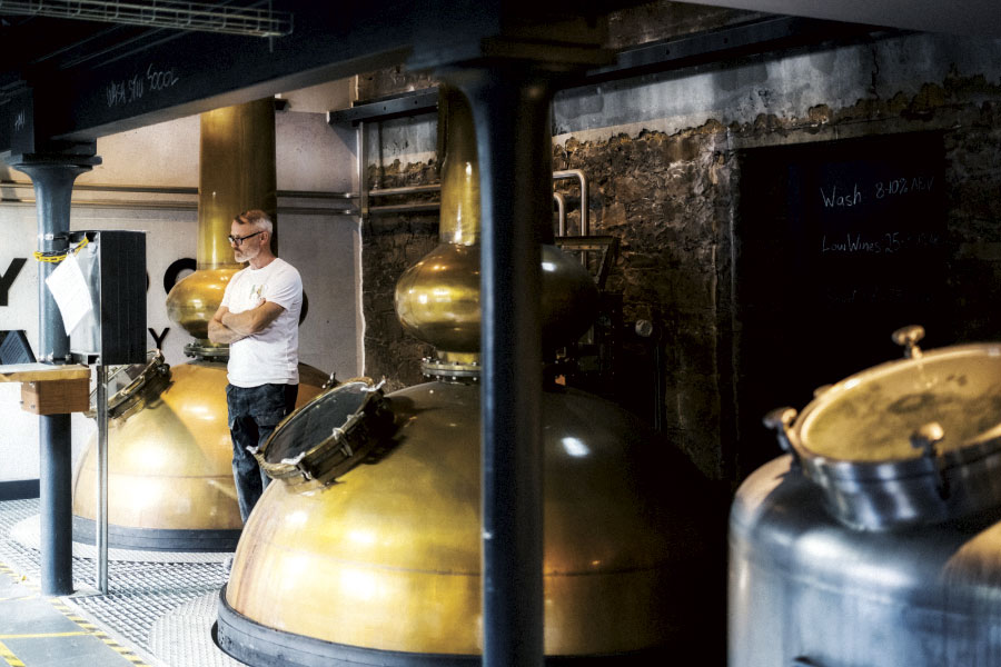 Distiller standing between large copper stills