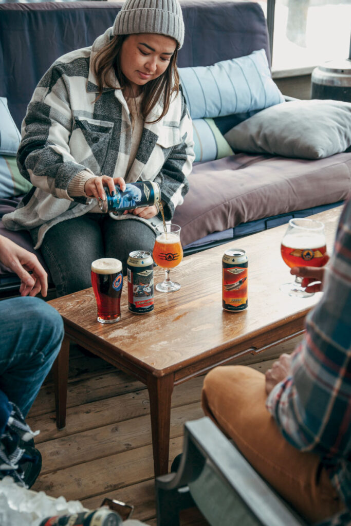 Young woman in heavy coat and toque pouring a glass of beer from a can