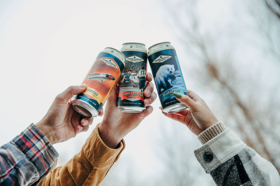 Three hands holding cans of beer up above their heads