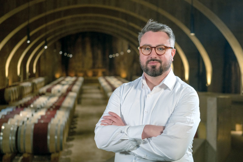 Taylor Whelan posing for photo with rows of wine barrels in background