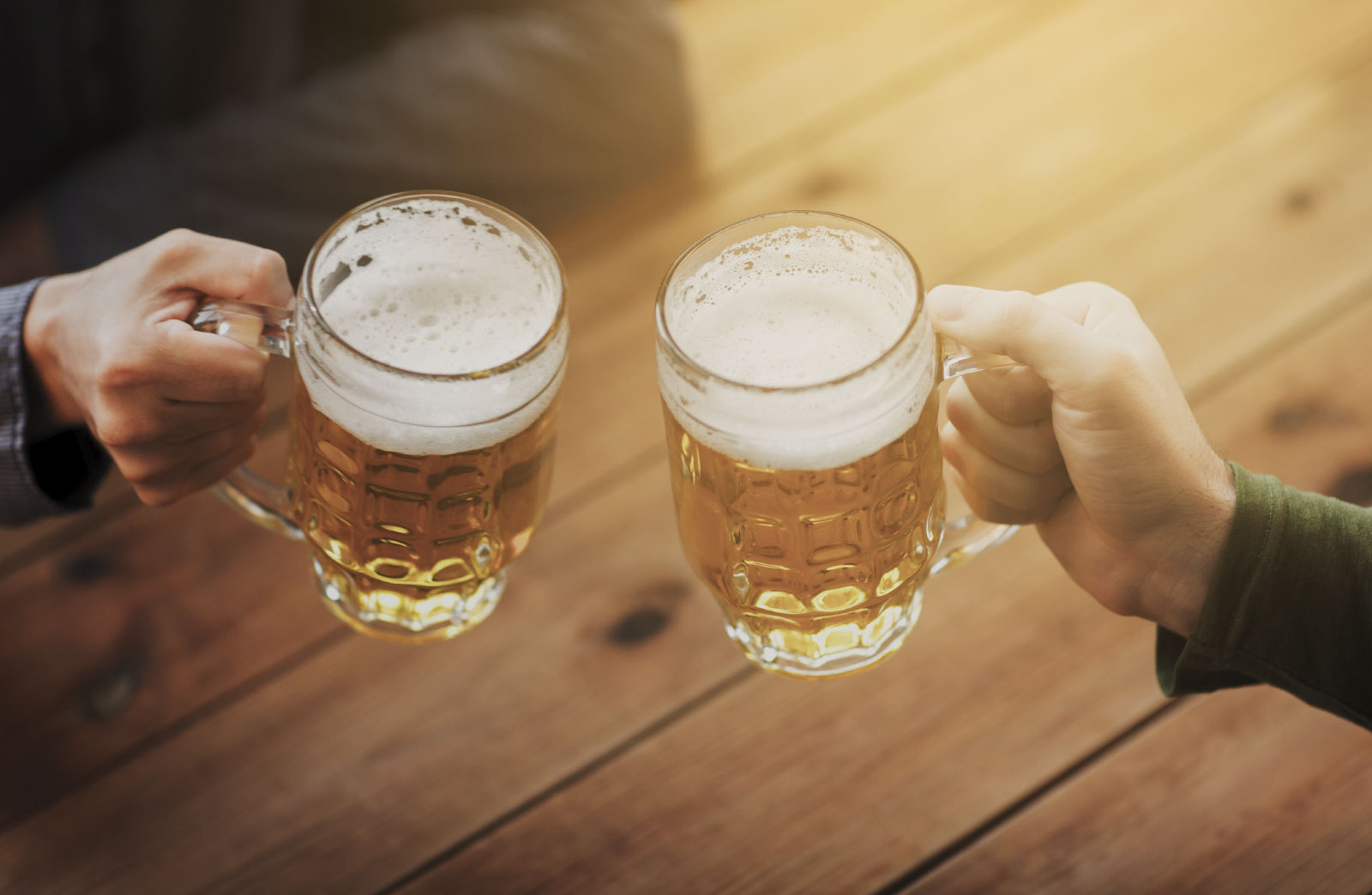close up of male hands clinking beer mugs at bar or pub