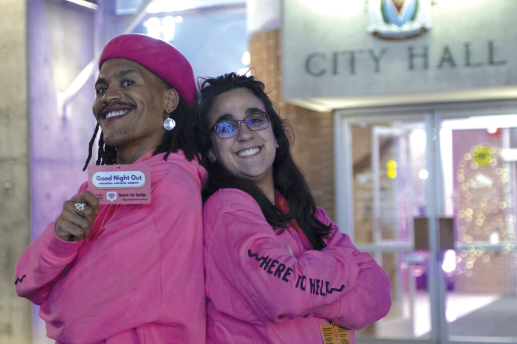 Couple wearing Good Night Out - We're Here to Help hooding, standing outside City Hall