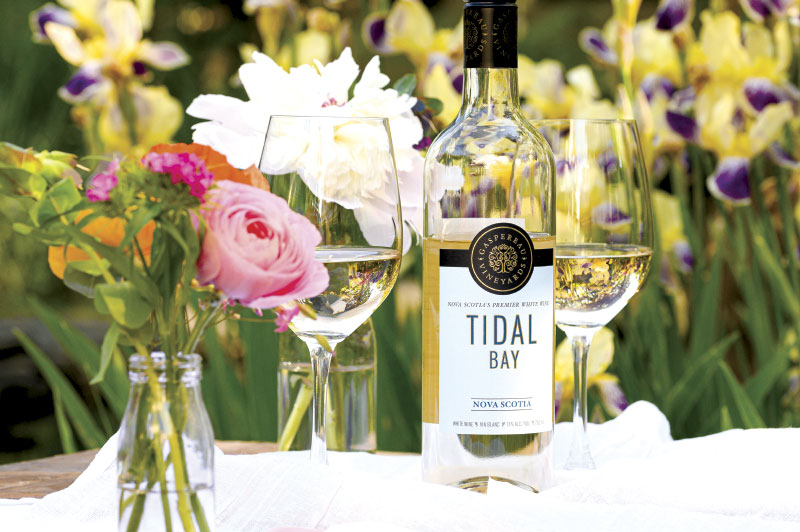 Bottle and glasses of Gaspereau Tidal Bay wine on table with flowers