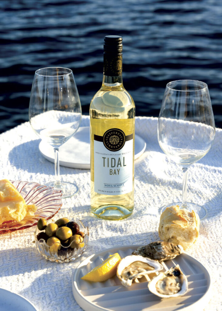 Bottle of Gaspereau Tidal Bay wine on table with plates of oysters and olives