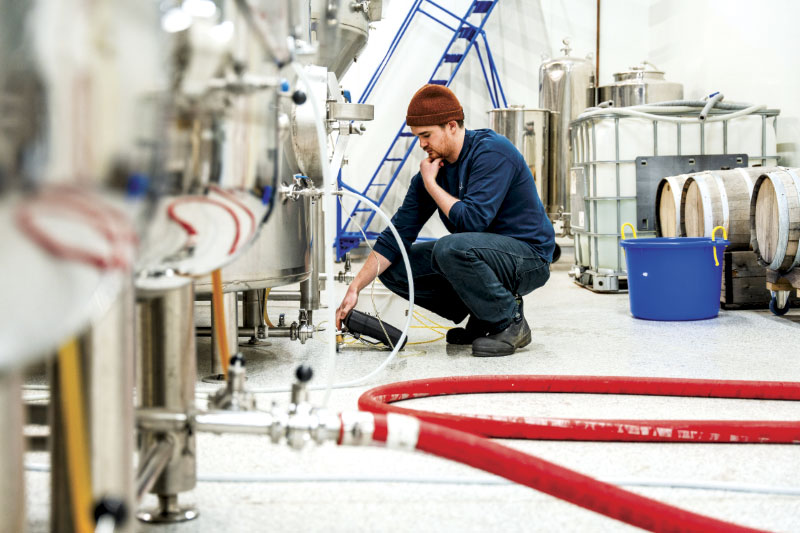 Man, crouched, inspecting brew tanks