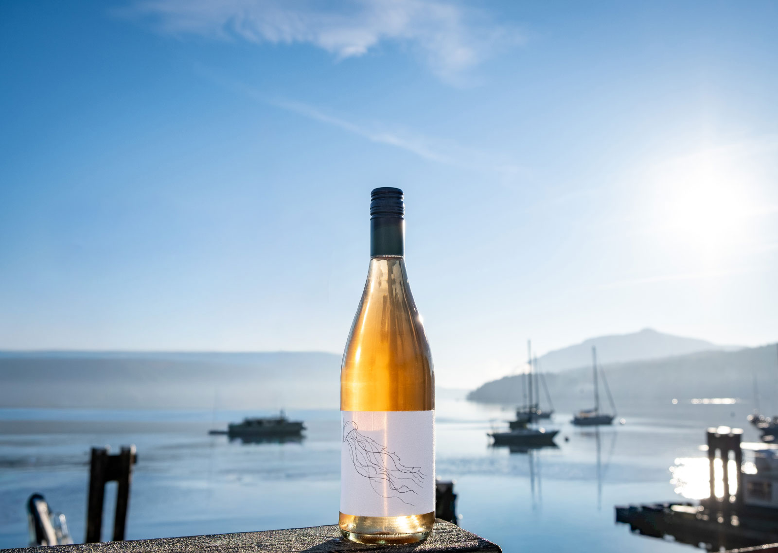 Bottle of wine on table with lake and bright, sunny sky in background