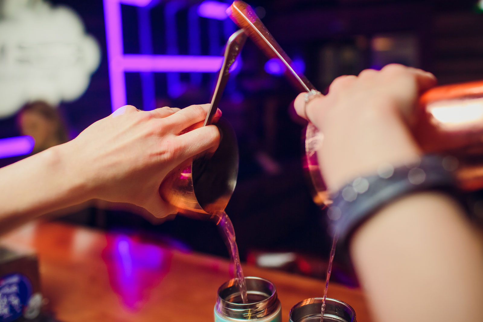 Bartender pouring contents of shakers into two glasses