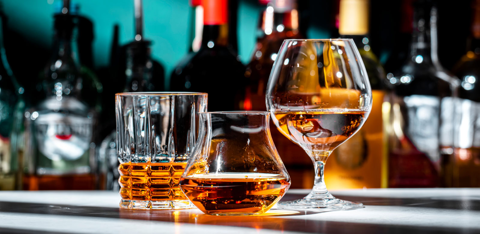Various glasses of whiskey with bottles in background