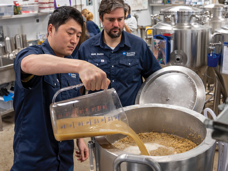 Students pouring liquid into large vat