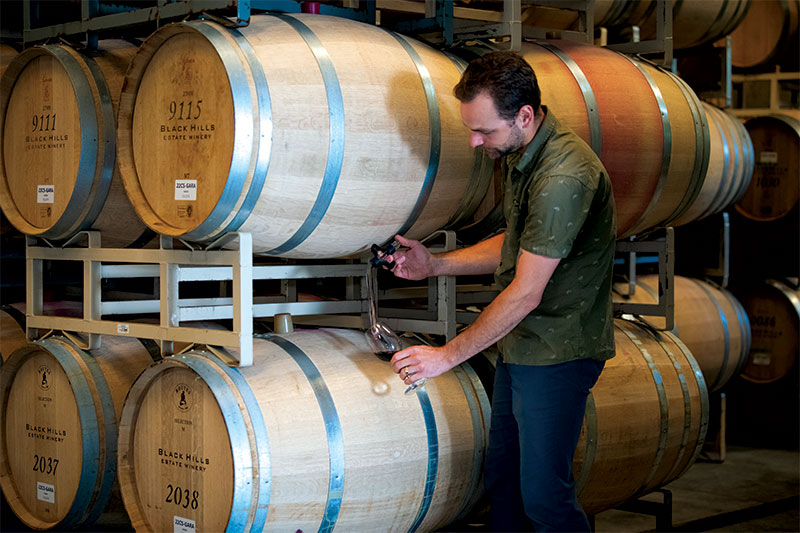 Ryan McKibbon pouring glass of wine from wooden barrel