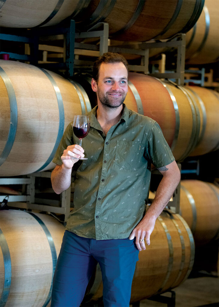 Ryan McKibbon holding glass of wine in barrel room