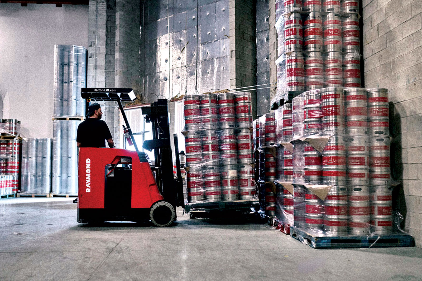 Worker in forklift stacks pallets of kegs