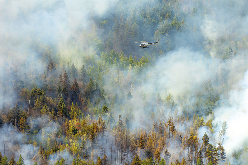 Rescue helicopter flying over a mountainside forest fire near Sparwood, British Columbia
