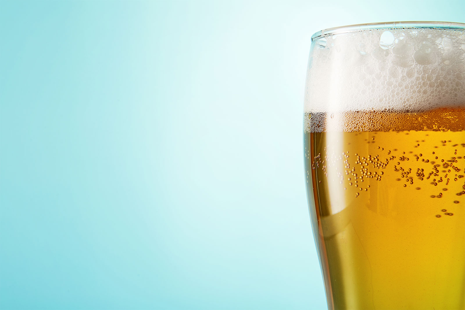 Closeup of glass of beer against light blue background