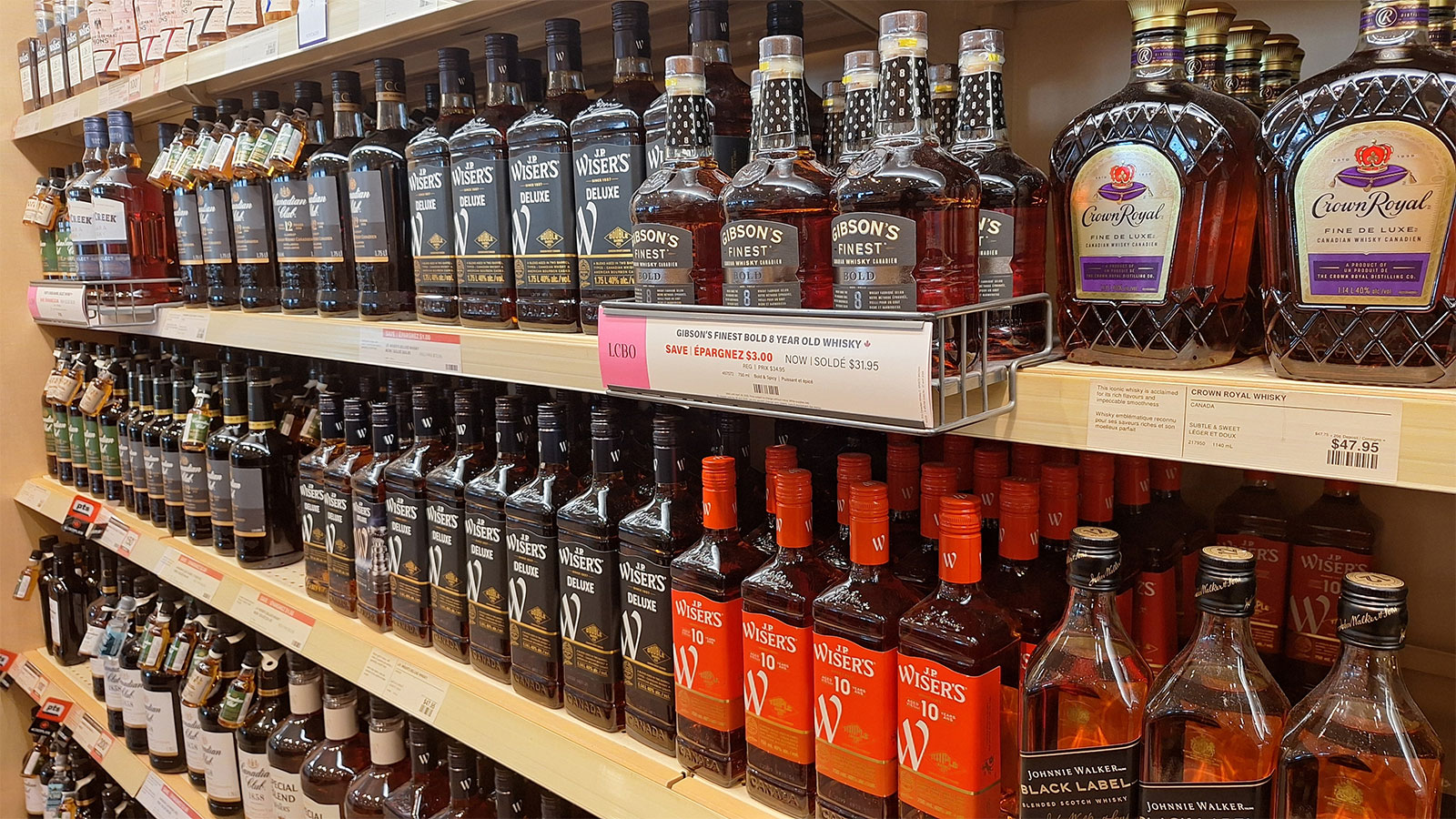 Close-up of whisky bottles on store shelves, including Wisers, Gibson's, and Crown Royal